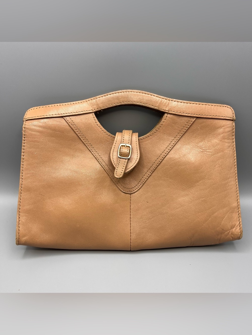 tan leather clutch featuring a built-in top cutout handle and a central buckled